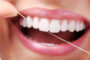 Image represents A smiling person cleaning her teeth and gums with dental floss