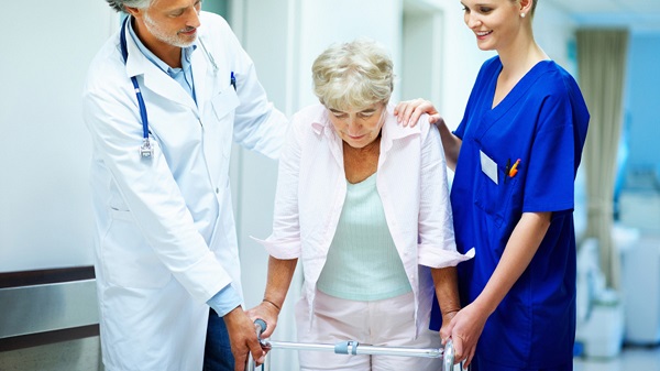 Smiling Nurse Helping Senior Lady To Walk Around The Nursing Home