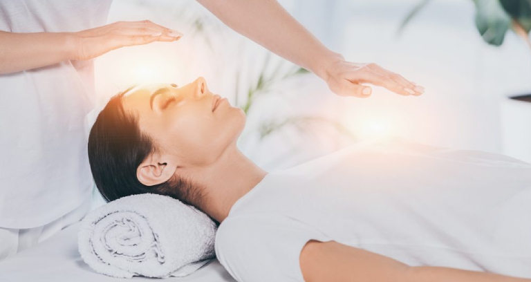 A Side View of Calm Young Woman Receiving Reiki Healing Therapy On Head And Chest.