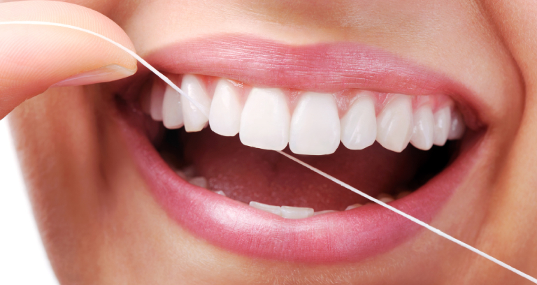 Image represents A smiling person cleaning her teeth and gums with dental floss